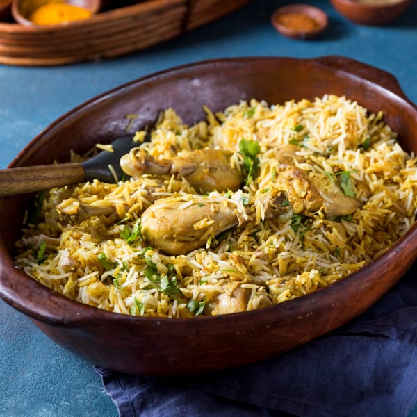 A large clay bowl filled with chicken biryani, garnished with fresh cilantro, on a blue surface.