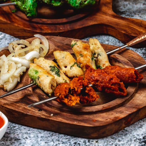 Two skewers of Indian kebabs, one red and one white, with sliced onions on a wooden board.