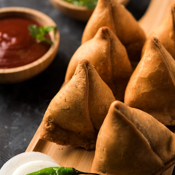 Golden-brown Indian samosas arranged on a wooden board with dipping sauces and fresh garnishes.