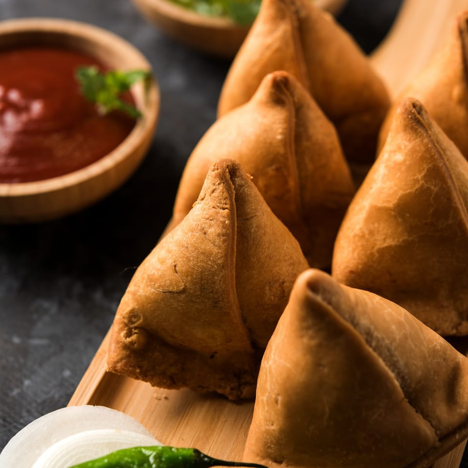 Golden-brown Indian samosas arranged on a wooden board with dipping sauces and fresh garnishes.