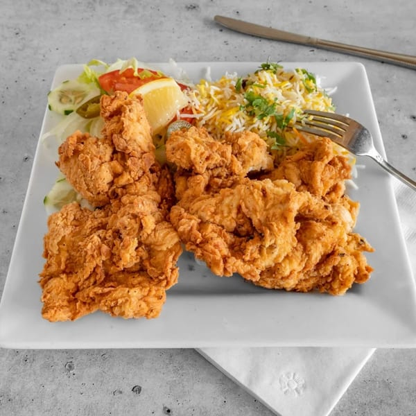 Crispy fried chicken pieces with basmati rice, salad, and a lemon wedge on a white plate.
