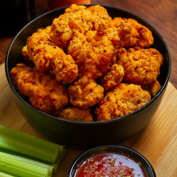 A black bowl filled with crispy golden chicken pakora, with celery sticks and dipping sauce.
